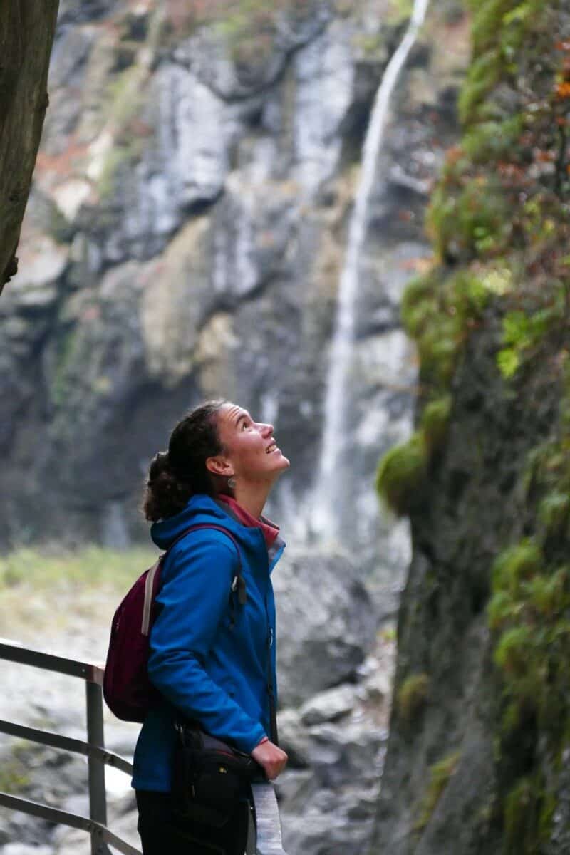 Femme admirant une cascade dans la nature avec un sac à dos bleu.